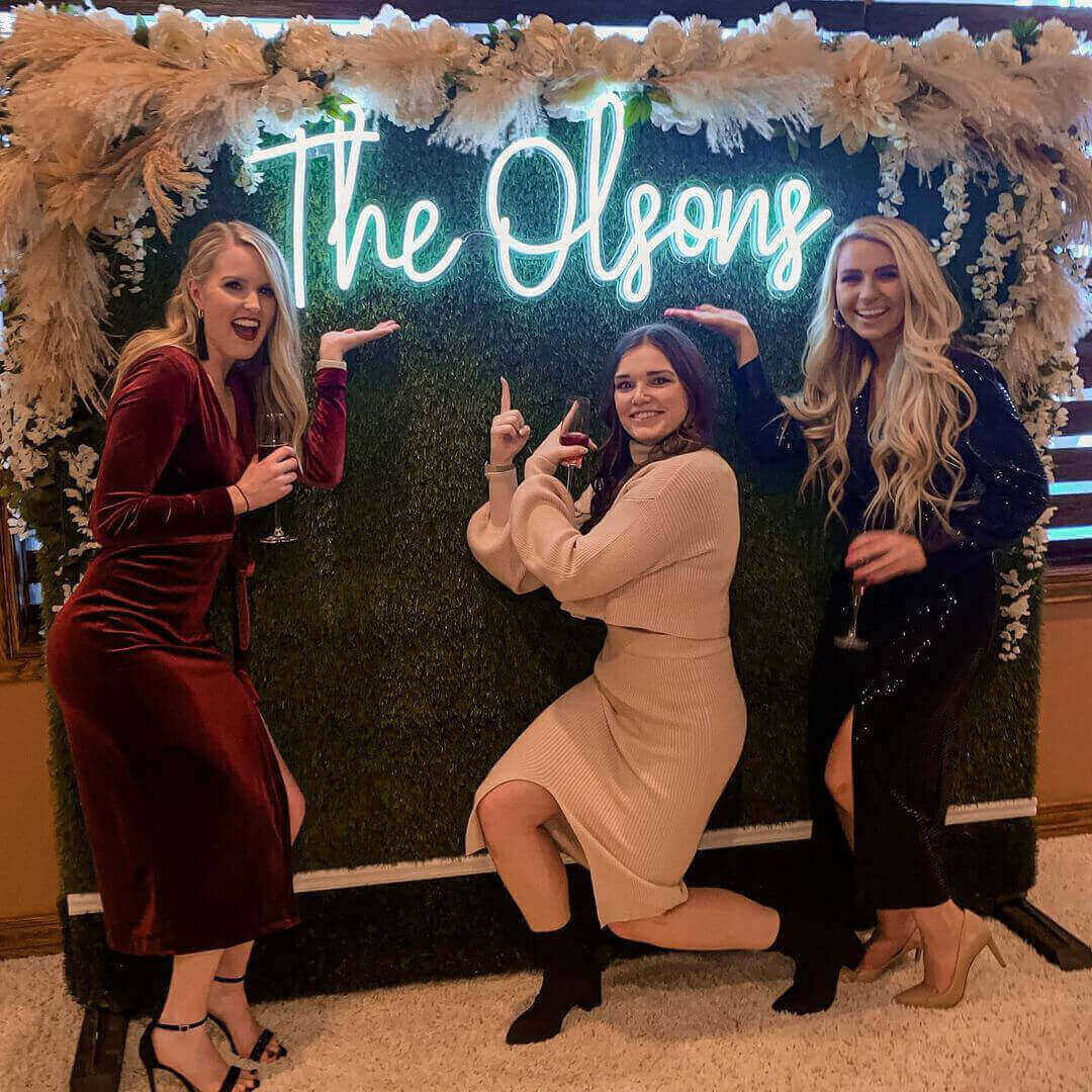 Guests taking picture in front of press wall with Turquoise The Olsons' last name wedding neon sign on it