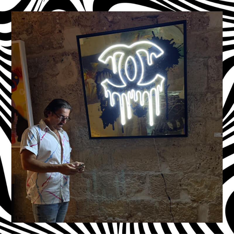 A person standing next to a white Chanel neon sign hanged on a wall