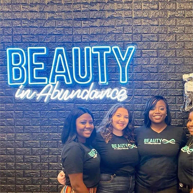 Employees standing in front of Beauty in abundance neon sign