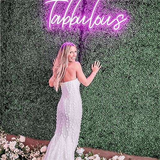 Bride leaning on press wall with Tabbulous wedding neon sign on it